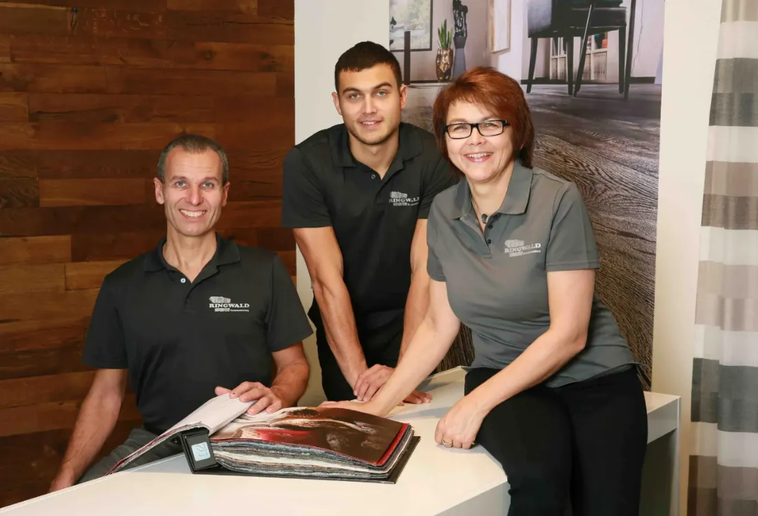 Ausschnitt der Website von Ringwald Raumausstattung, Landkreis Emmendingen: Echtes Teamfoto in Arbeitskleidung am Beratungstisch — der Besucher sieht konkrete Ansprechpartner statt Stockbilder.